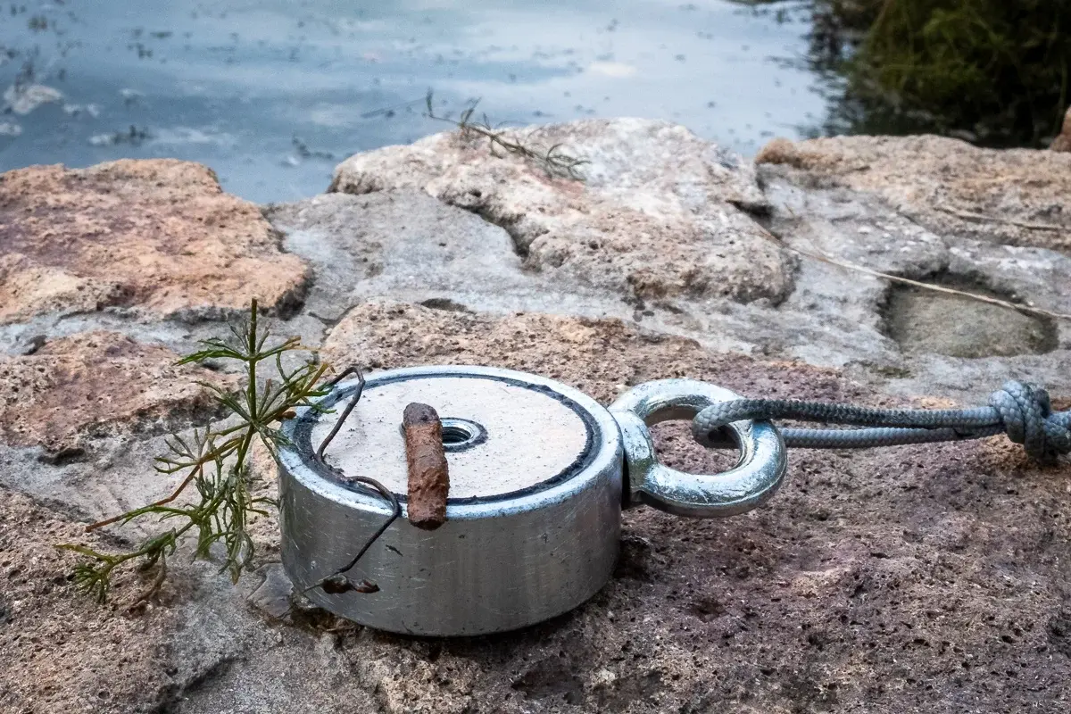 Aimant de pêche avec une trouvaille métallique accrochée, au bord de l'eau